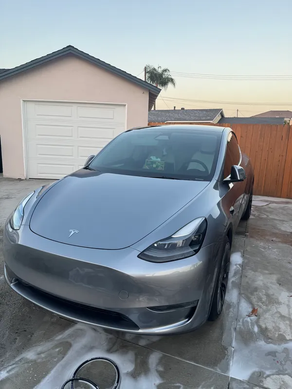 Clean grey Tesla Model Y after a hand wash, front three-quarter view on a driveway at dusk