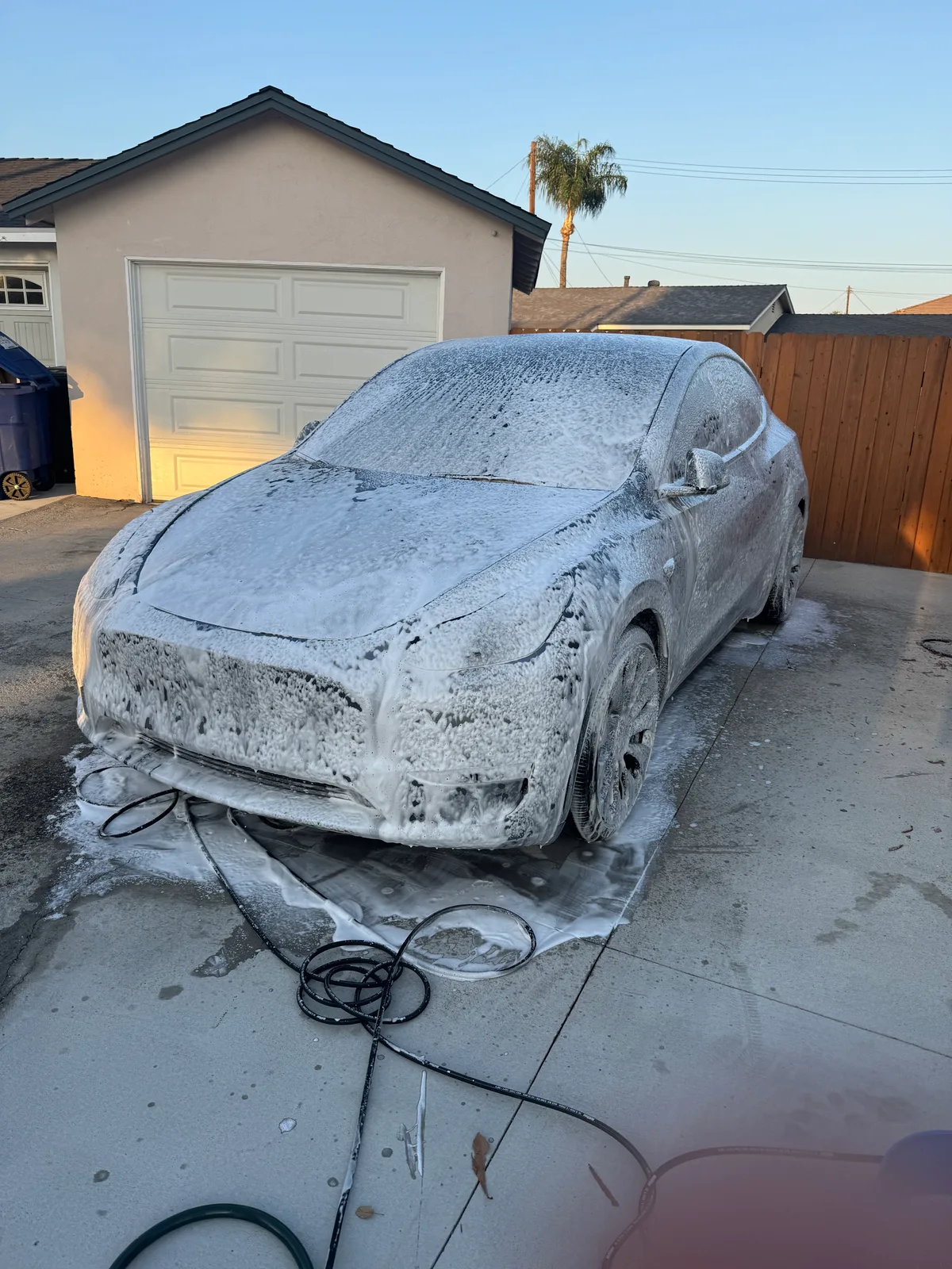Grey Tesla Model Y covered in thick white foam pre-soak on a residential driveway before the hand wash