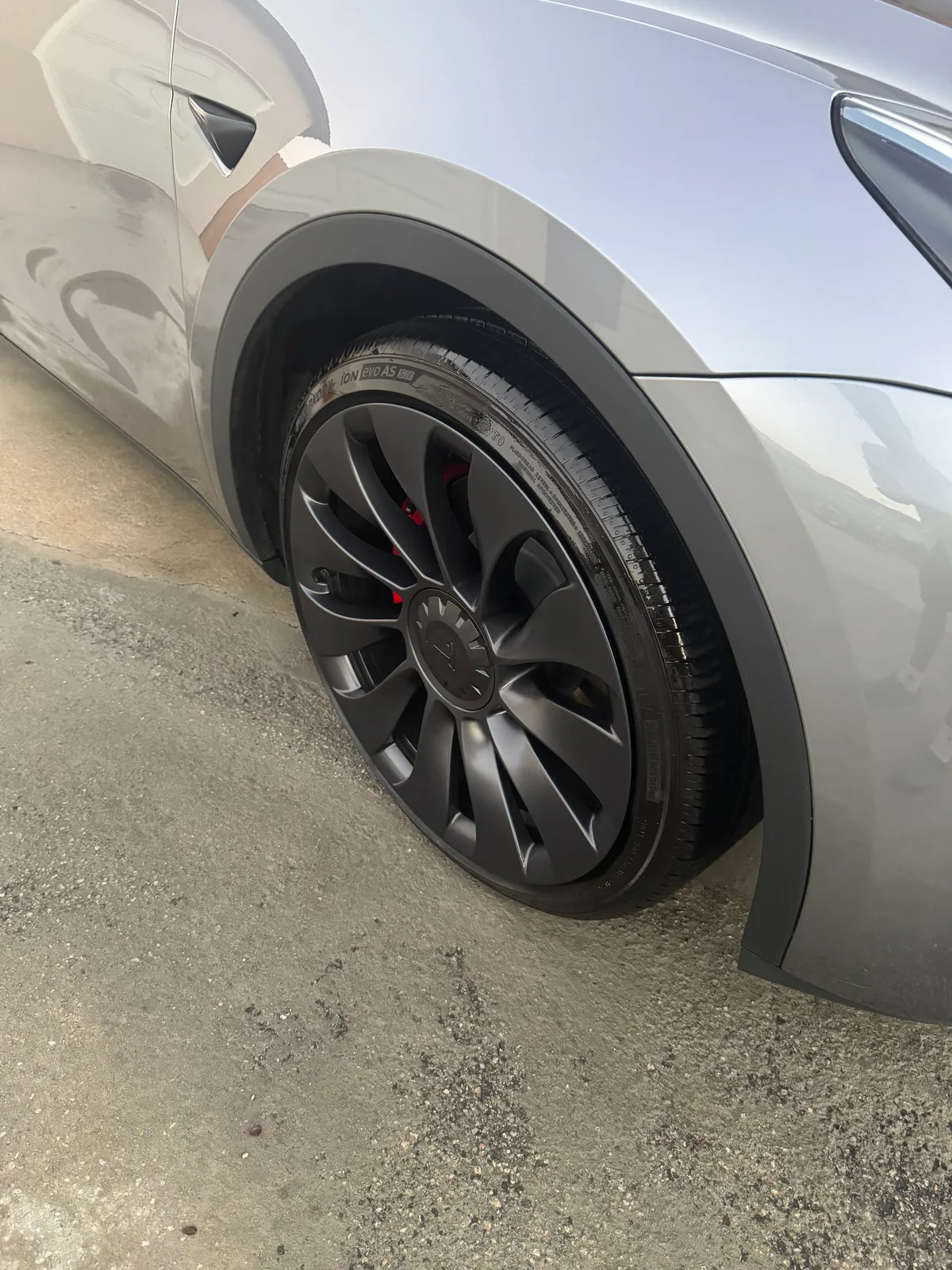 Close-up of a cleaned black alloy wheel and dressed tire on a grey Tesla after a hand wash
